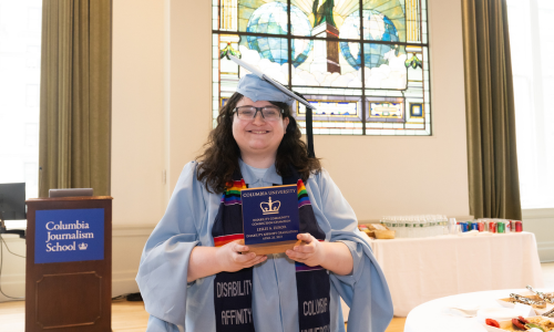 Leslie Zukor smiling, wearing regalia, and holding certificate of achievement at the Disability Affinity Graduation