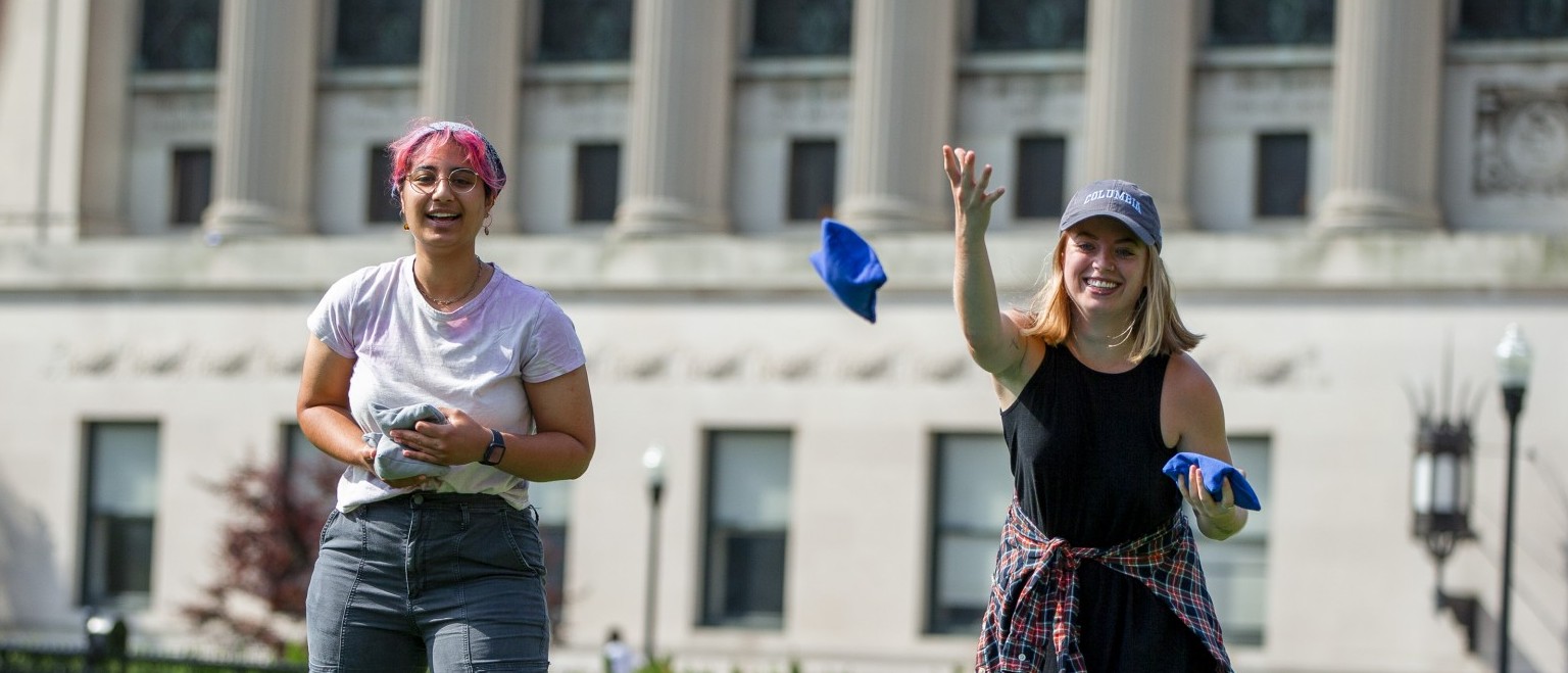 two students play cornhold - bean bag in midair