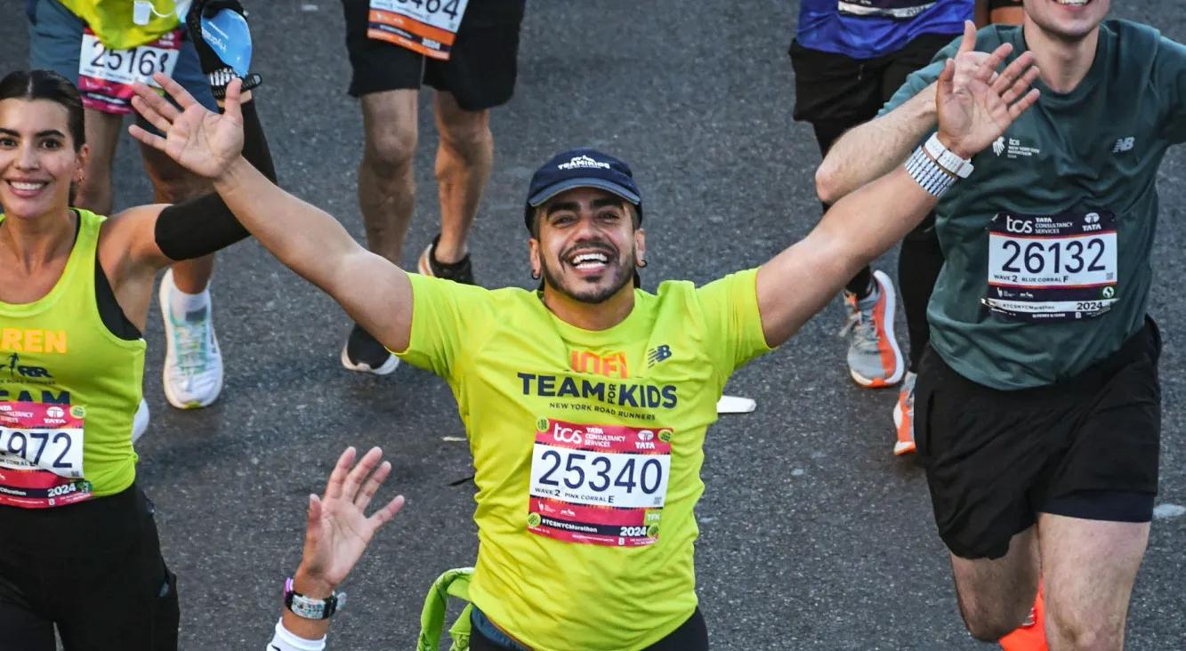 Joel Teron (GS'27) lifting his arms while running and smiling during a marathon race. 