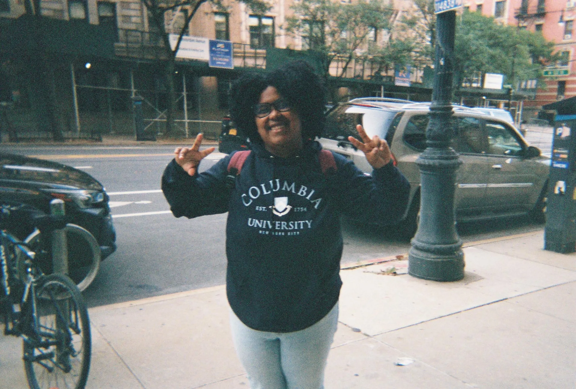 Giovanna Corcino is standing and holding up two peace signs with her fingers and she is smiling 
