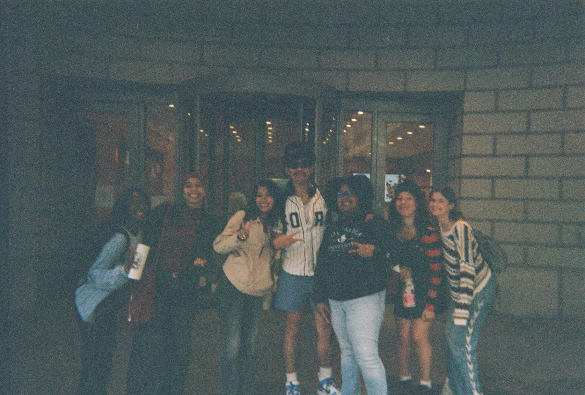 From left to right; Makeda Byfield, Lalia Salem, Dyana Reyes, Allan Zheng, Giovanna Corcino, Marley Chavarria and Keely Haw standing in front of the Columbia School of Social Work with smiles and holding peace signs. 