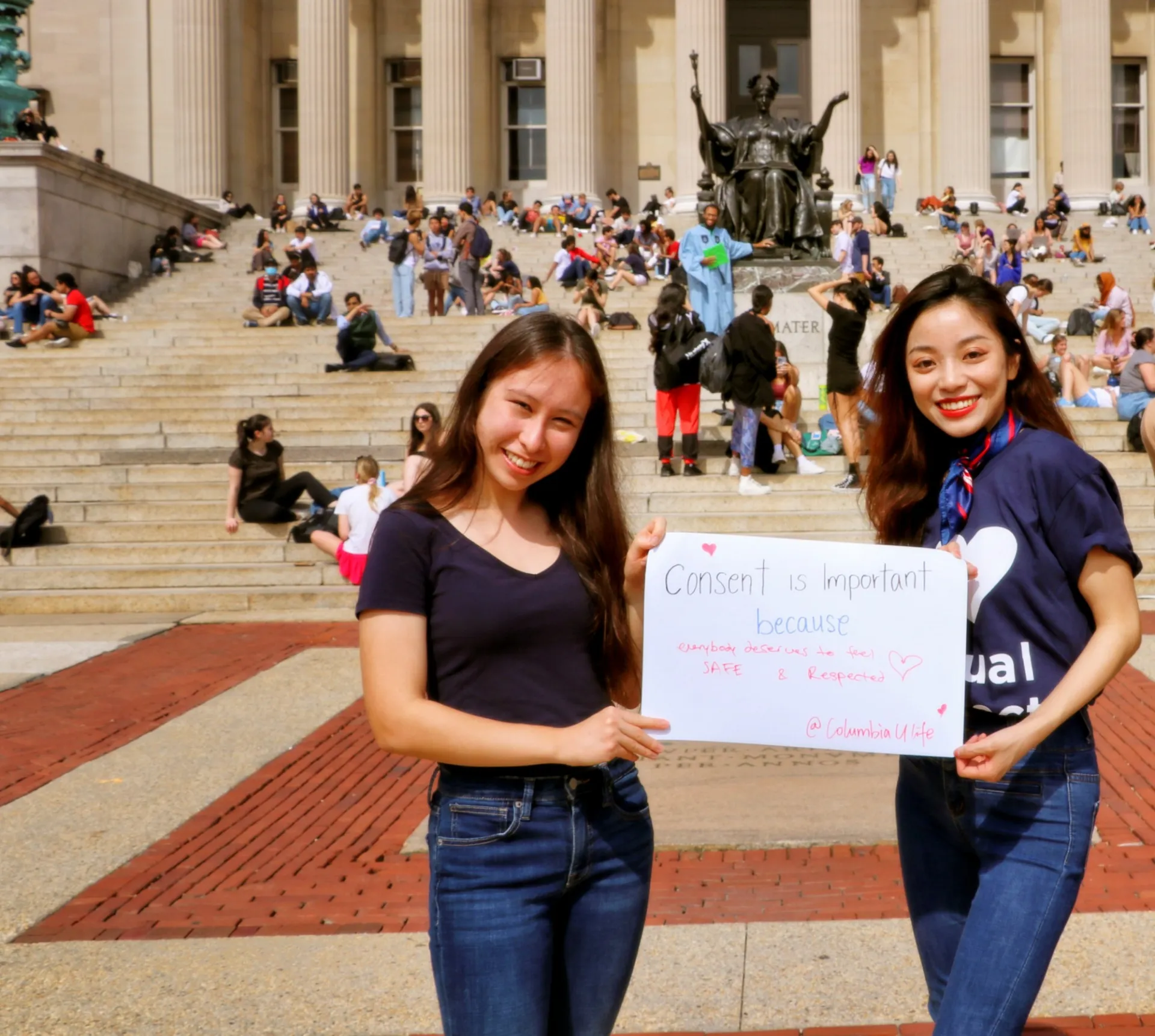 Hanyu with another University Life Ambassador holding a sign that says "Consent is important because everyone deserves to feel safe."