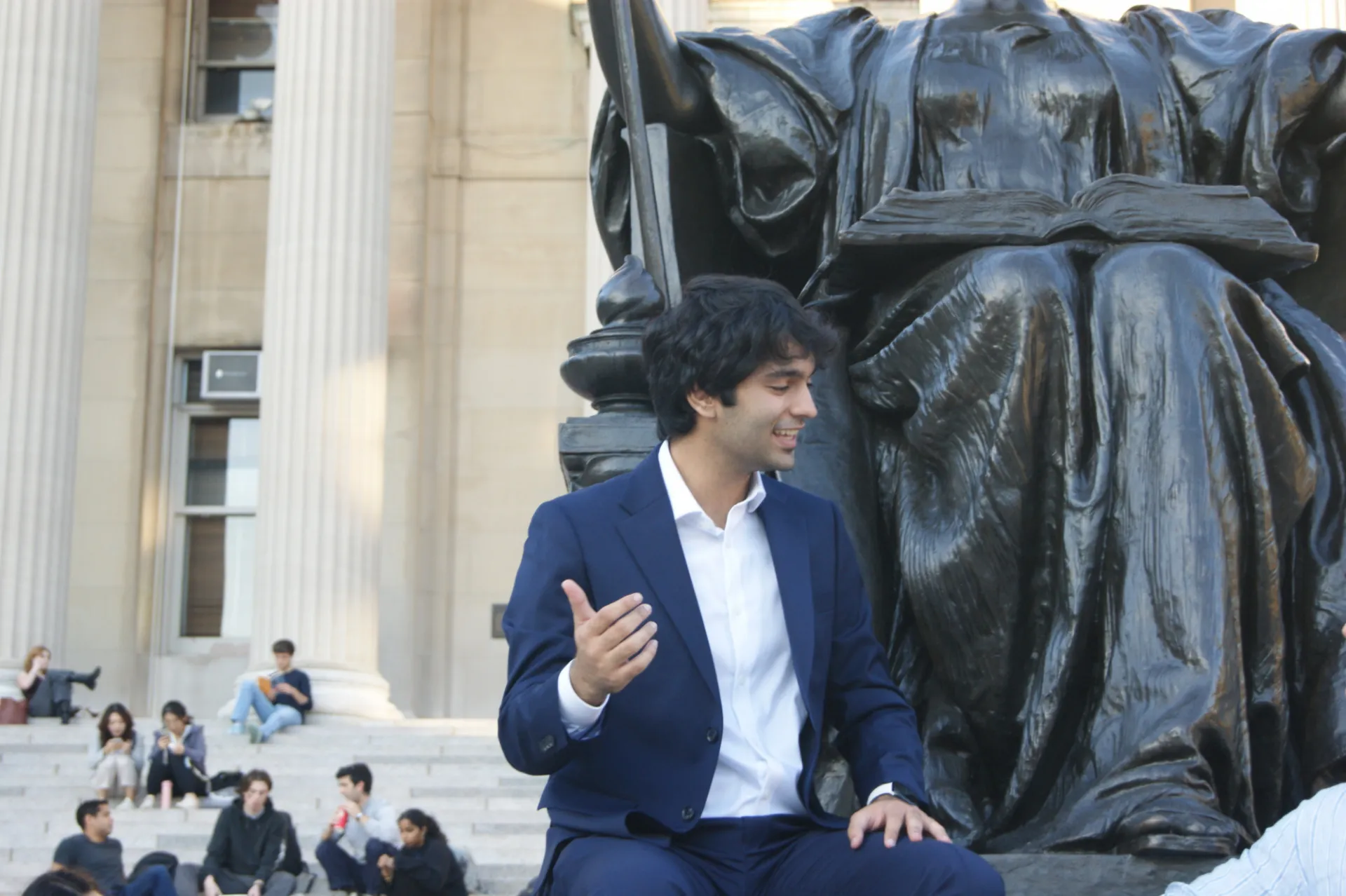 Haris Shah sitting beneath the Low Library Statue talking to a person beside him.